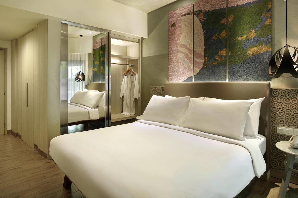 A hotel room with a large bed, a wardrobe, a bathroom with a shower, and a wall with a colorful abstract painting.