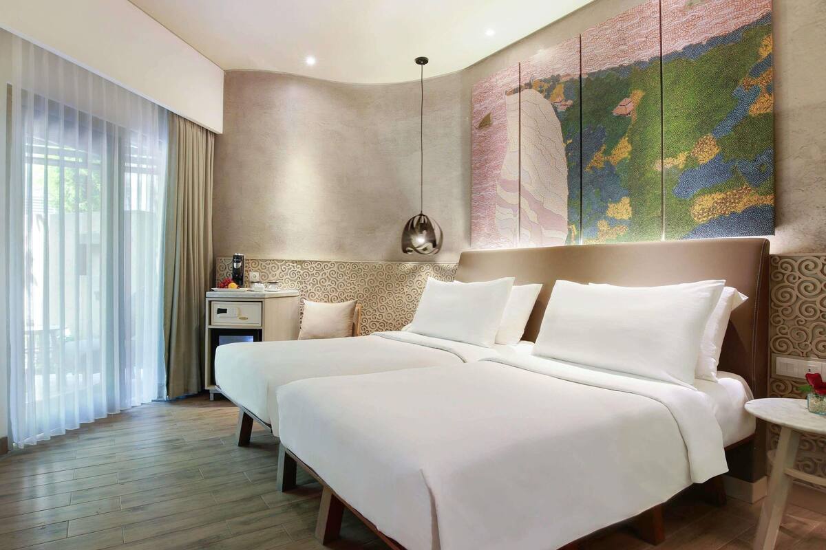 A hotel room with a large bed, a bedside table, a lamp, and a large abstract painting on the wall.