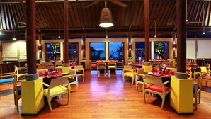 Un restaurant spacieux doté d’un plancher en bois, de hauts plafonds et de grandes fenêtres. Les tables sont dressées avec des serviettes rouges et des nappes blanches.