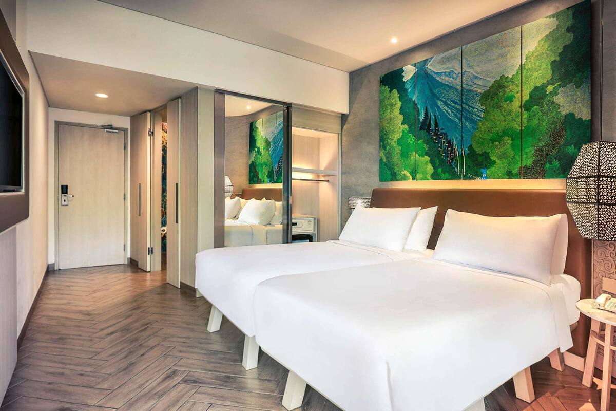 A modern hotel room with a large bed, a painting on the wall, and a wooden floor.