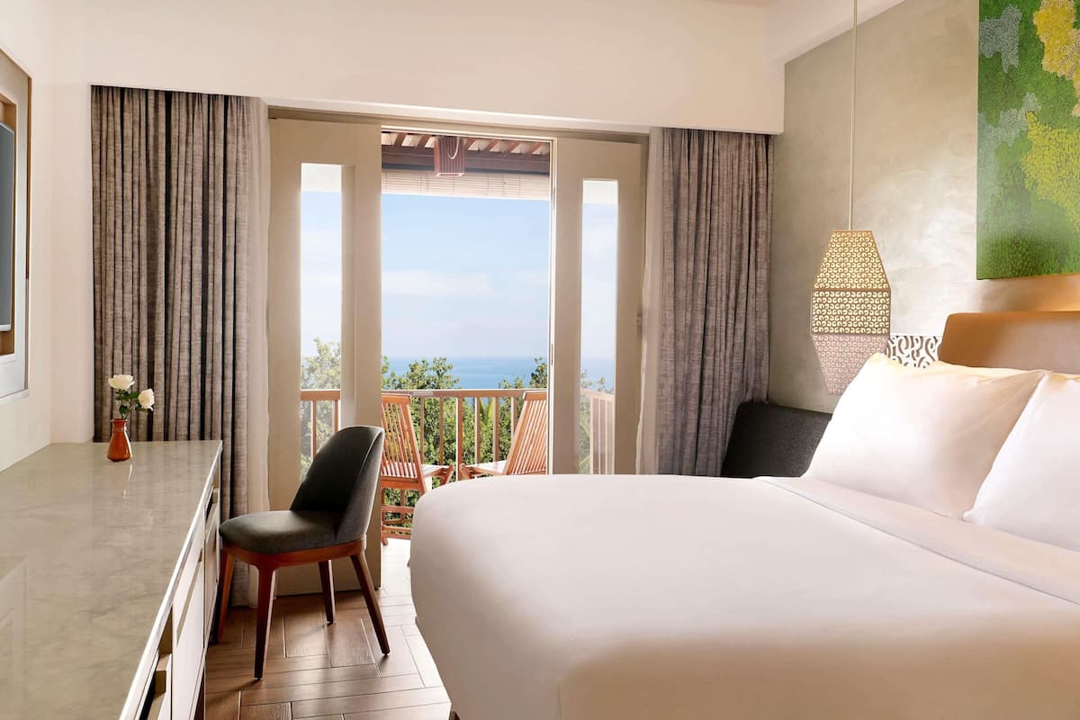 A hotel room with a bed, a desk, a chair, and a view of the sea.