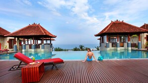 Un espace aménagé au bord de la piscine, avec des chaises longues rouges, une terrasse en bois et une vue sur l’océan.