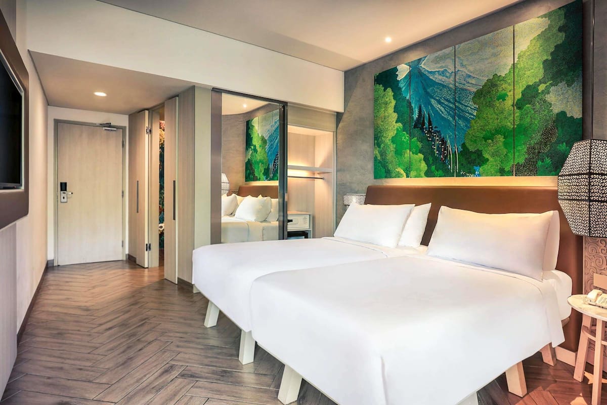 A hotel room with a large bed, a painting on the wall, and a wooden floor.