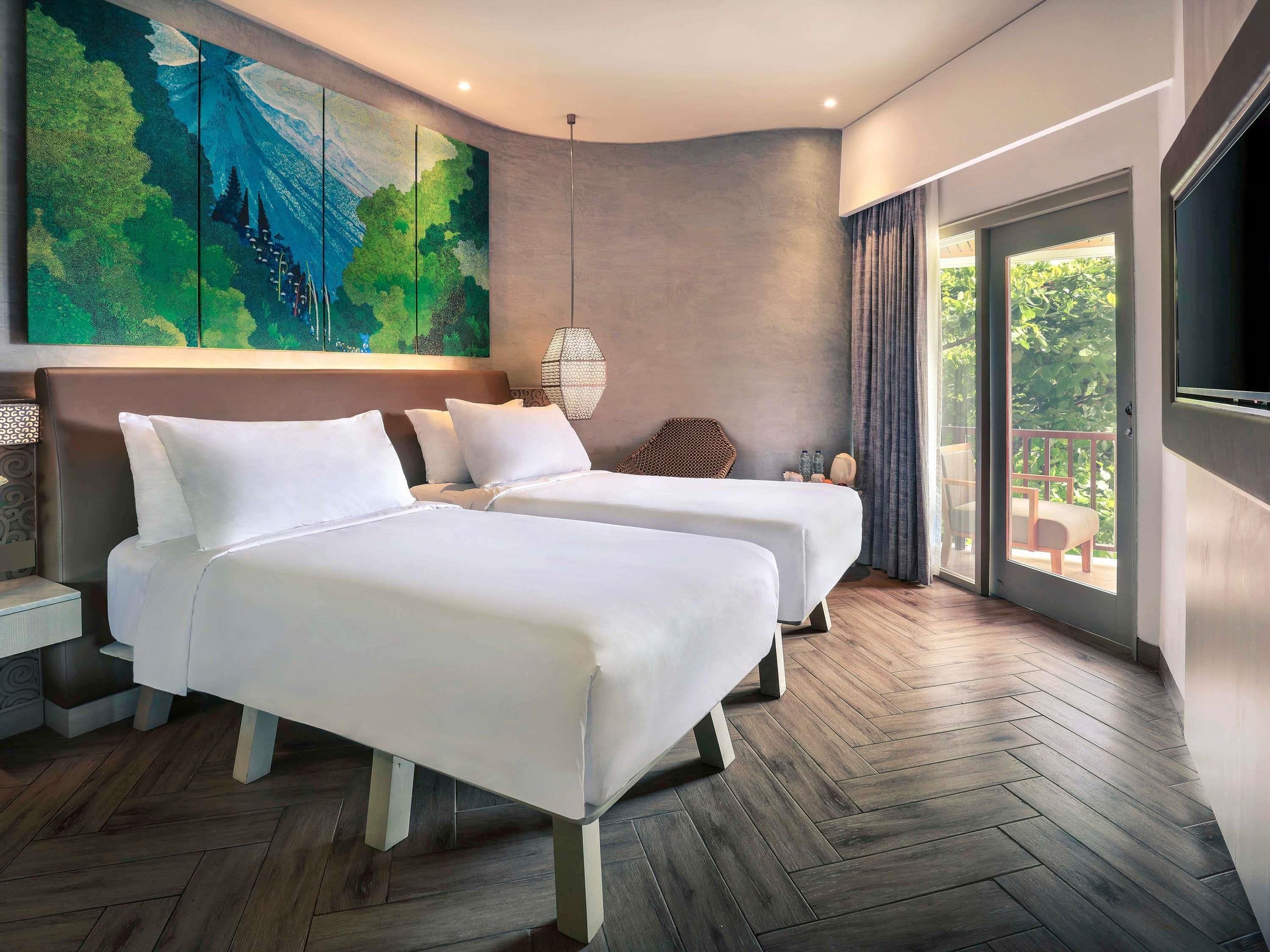 Une chambre d’hôtel moderne avec deux lits, un grand tableau, un balcon avec vue et un téléviseur fixé au mur.