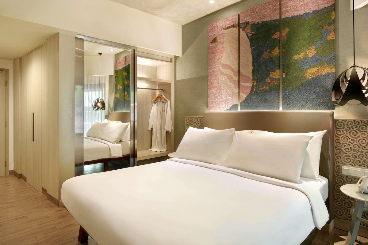 A hotel room with a large bed, a walk-in closet, a robe hanging, and a wall with a colorful abstract painting.