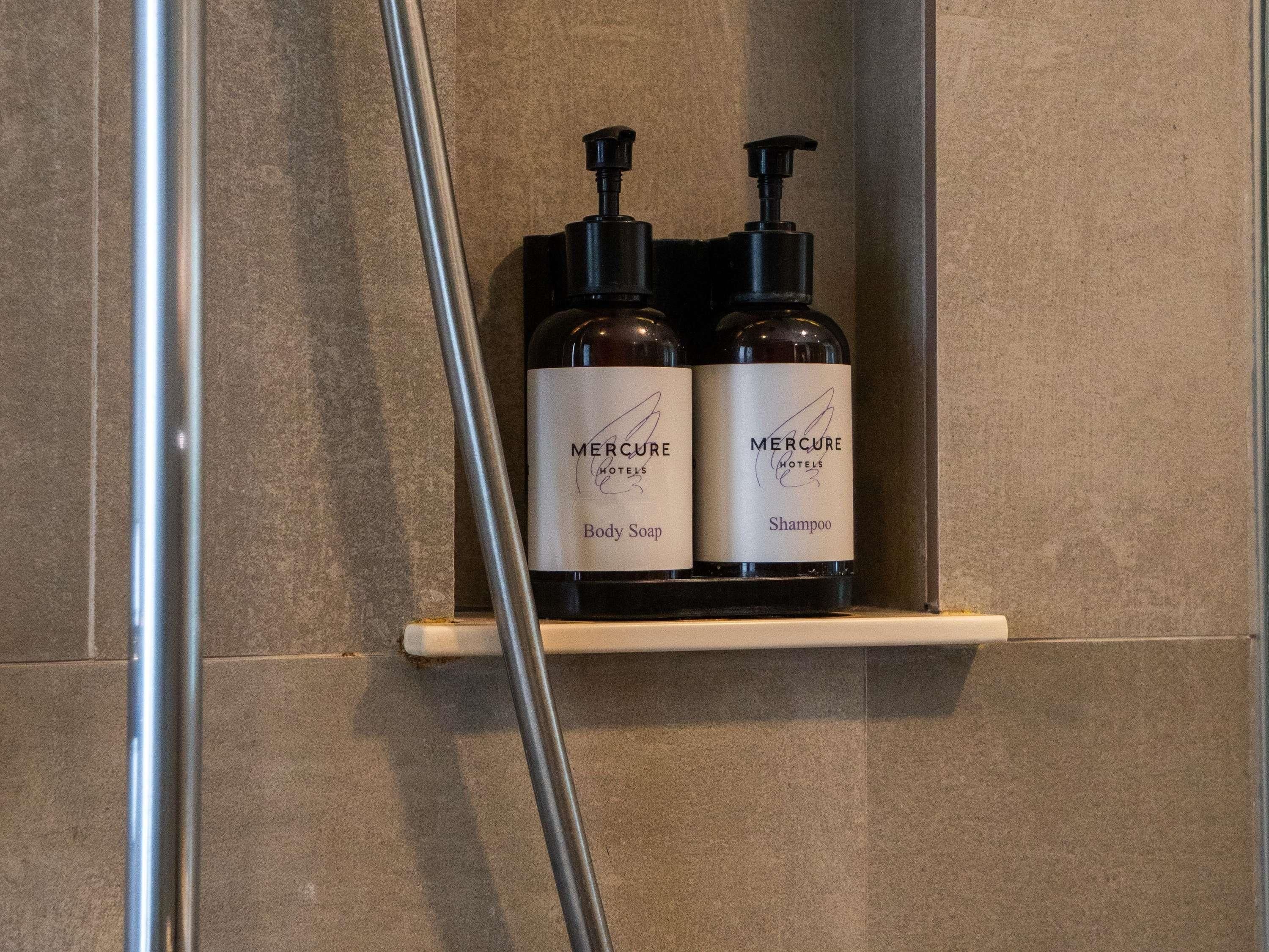 Un estante en el baño con dos botellas de jabón y champú Mercure.