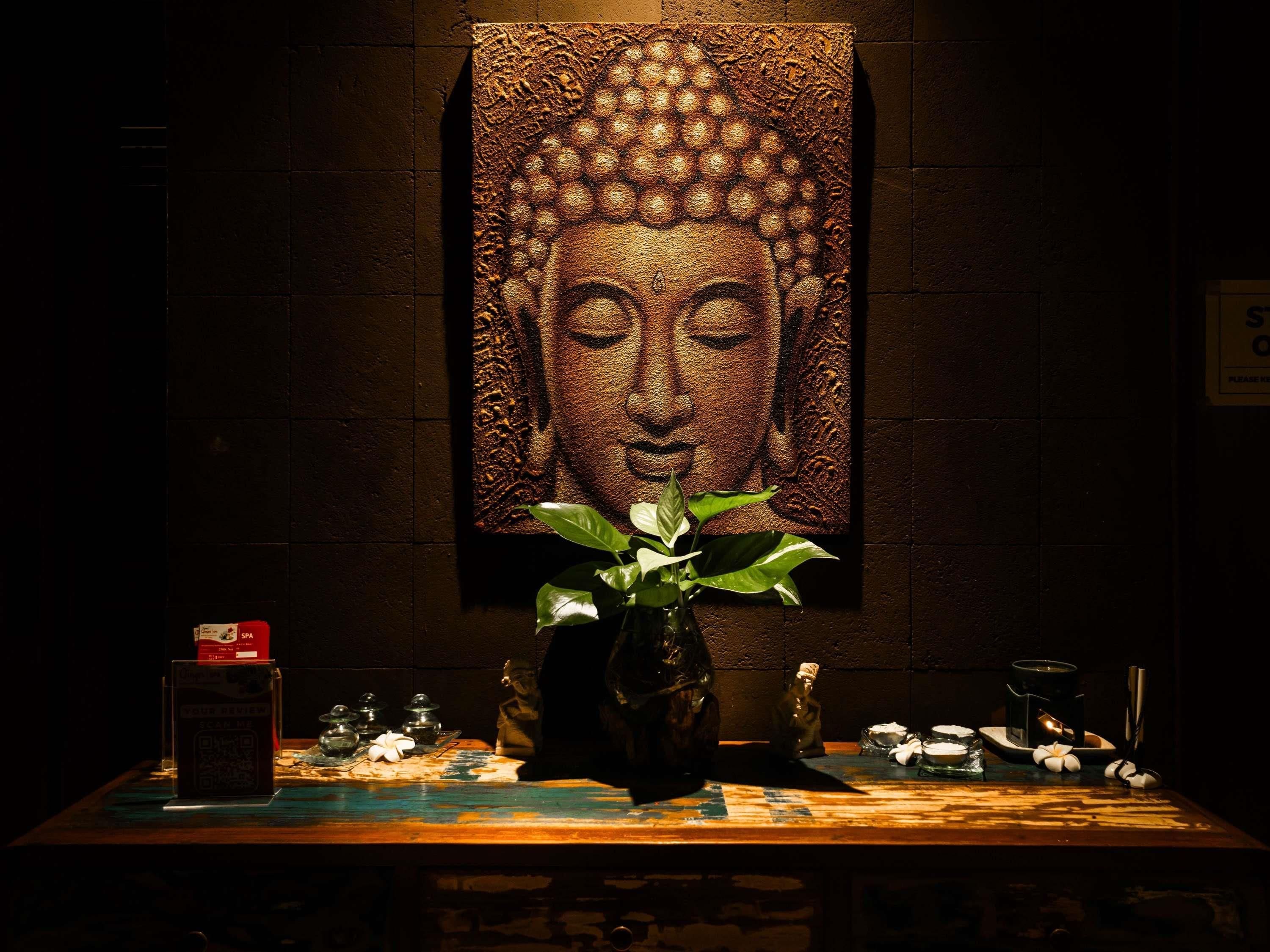 A room with a Buddha statue, a plant, and a table with various items.