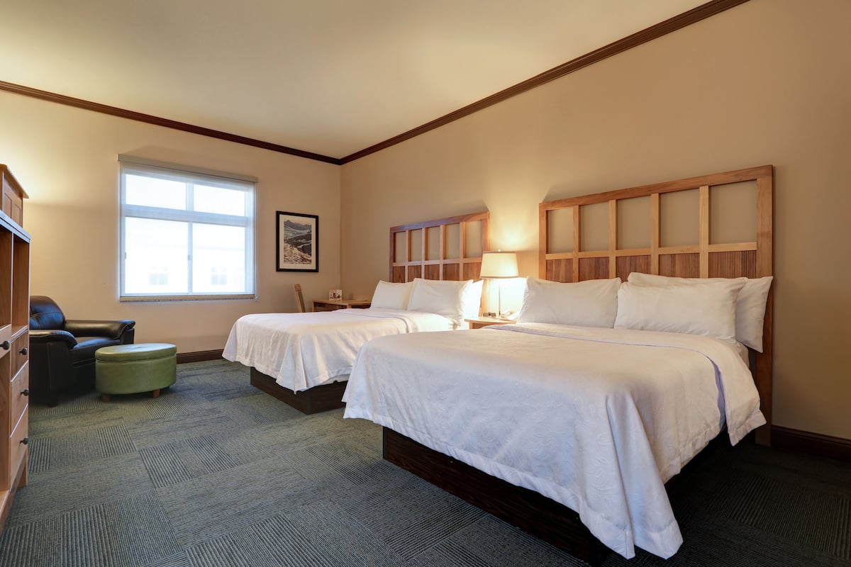 A hotel room with two beds, a desk, a chair, a window, and a carpeted floor.