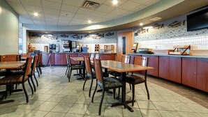A restaurant with multiple tables and chairs, a kitchen area, and a tiled floor. - Dimond Center Hotel (Anchorage)