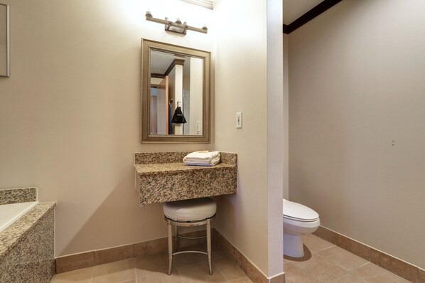Une salle de bain avec un comptoir en granit, des toilettes blanches et un petit tabouret.
