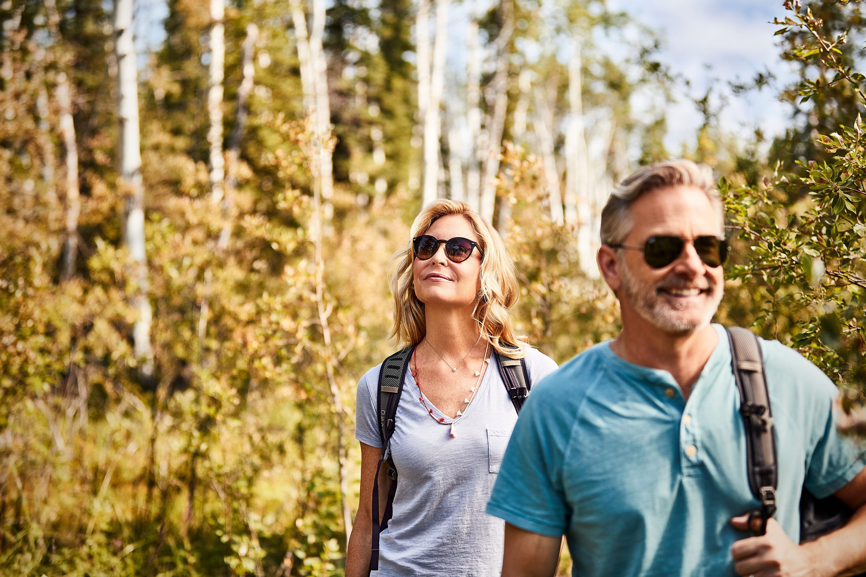 Two people standing in a forested area with trees and greenery in the background.