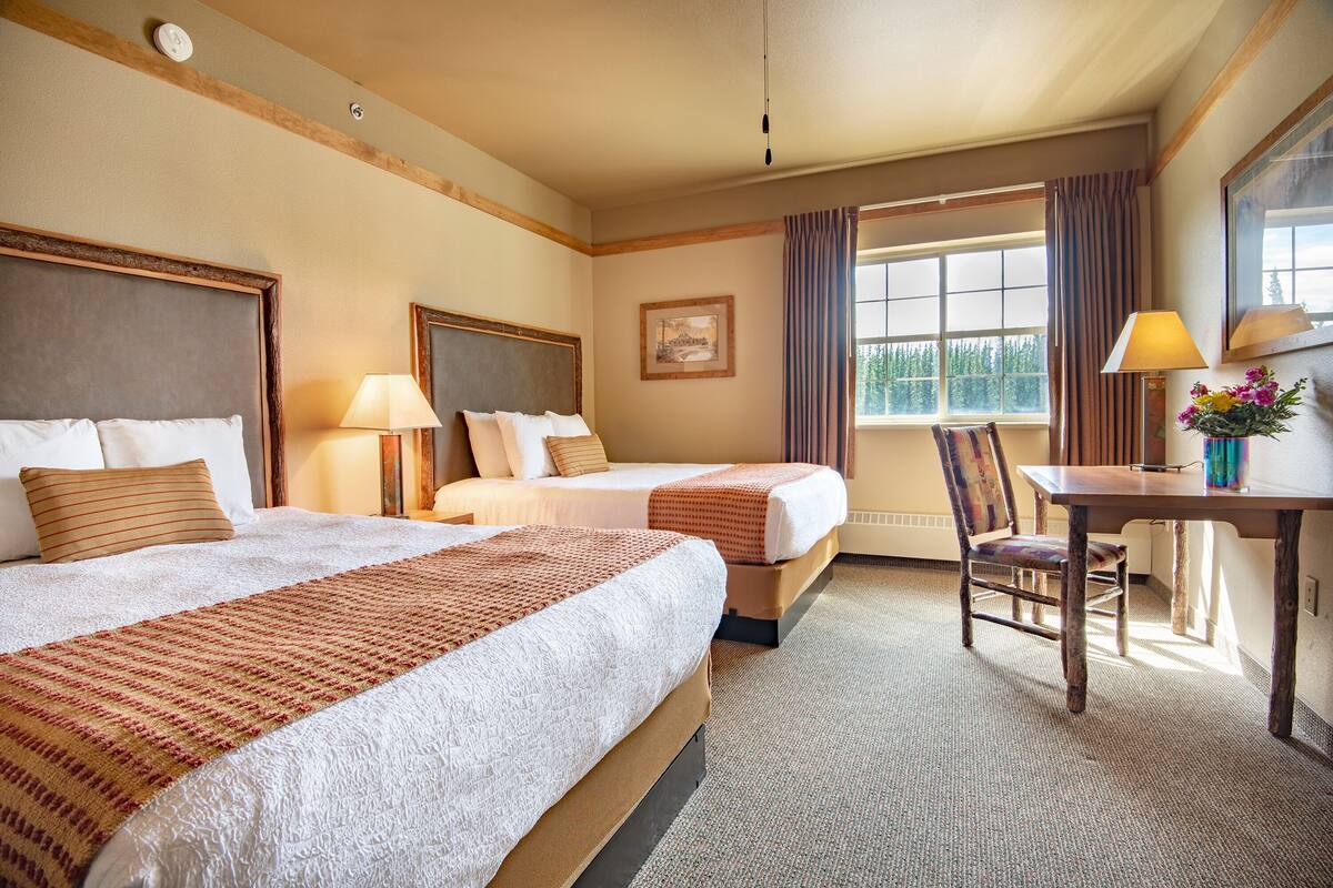 A hotel room with two beds, a desk, and a chair.