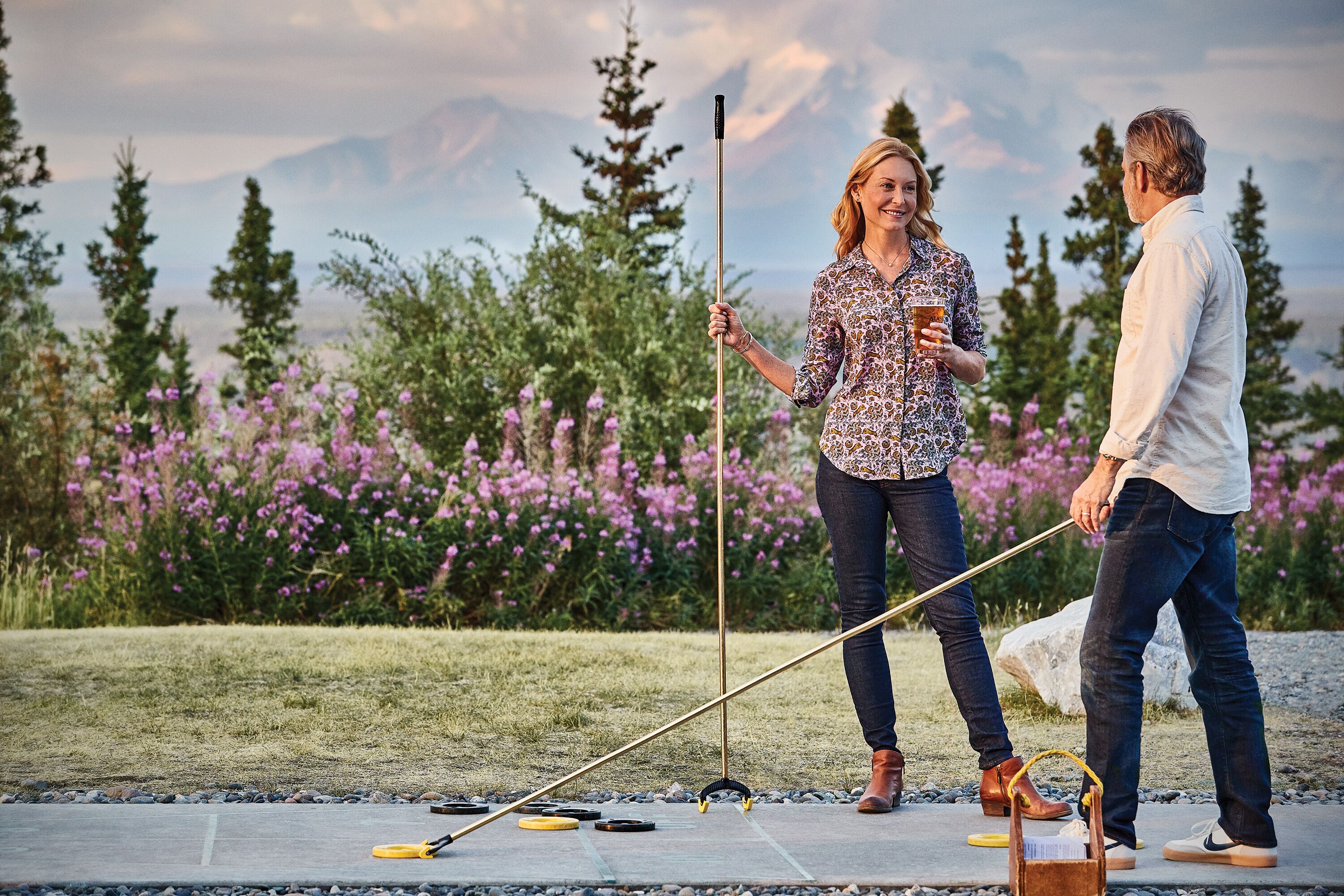 A couple playing croquet outdoors with a scenic mountain backdrop.