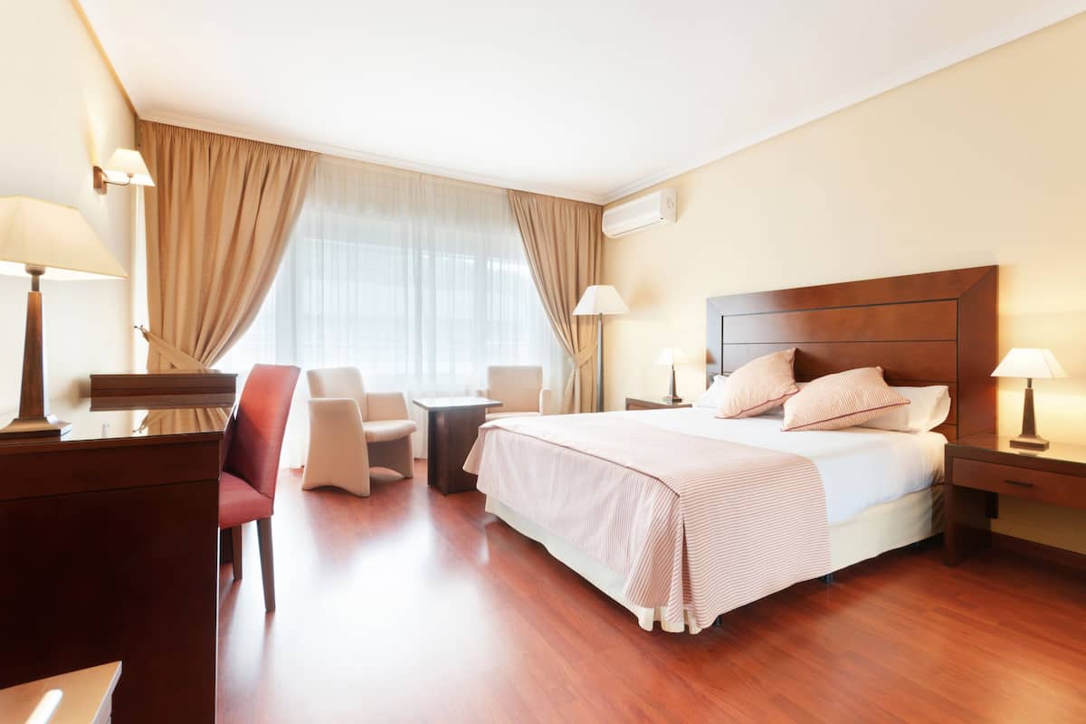A hotel room with a large bed, two bedside tables, a desk, a chair, and a window with curtains.