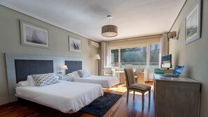 Une chambre d’hôtel avec deux lits, un bureau, une chaise et une grande fenêtre.