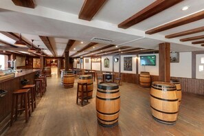 A bar area with wooden barrels, stools, and a television screen. - Hotel Nayade (Vegas de Matute)