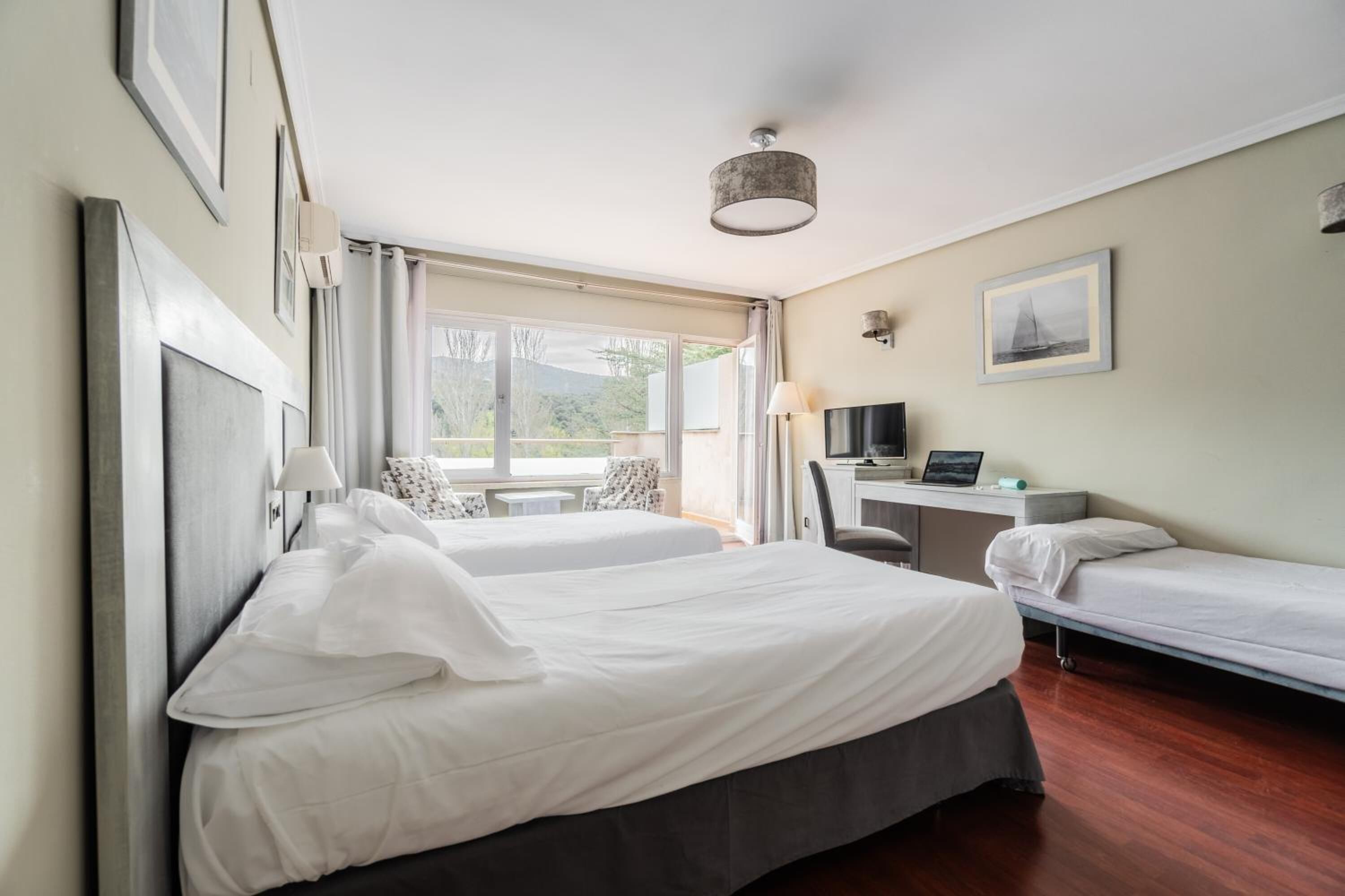 Une chambre d’hôtel avec deux lits, un bureau, une chaise, une télévision et une fenêtre donnant sur un paysage verdoyant.