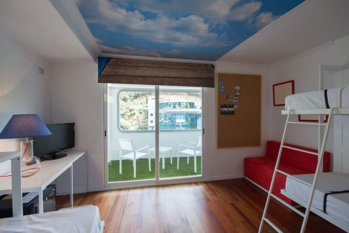 A room with a TV, bunk beds, a desk, and a sliding glass door to a balcony.