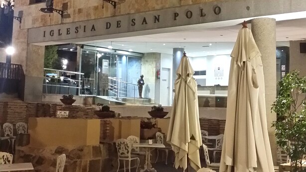 Un espacio al aire libre con mesas y sillas frente a un edificio que dice "IGLESIA DESAN POLO".