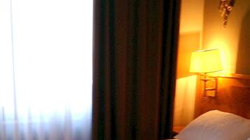 A hotel room with a bed, a lamp, and a curtain.