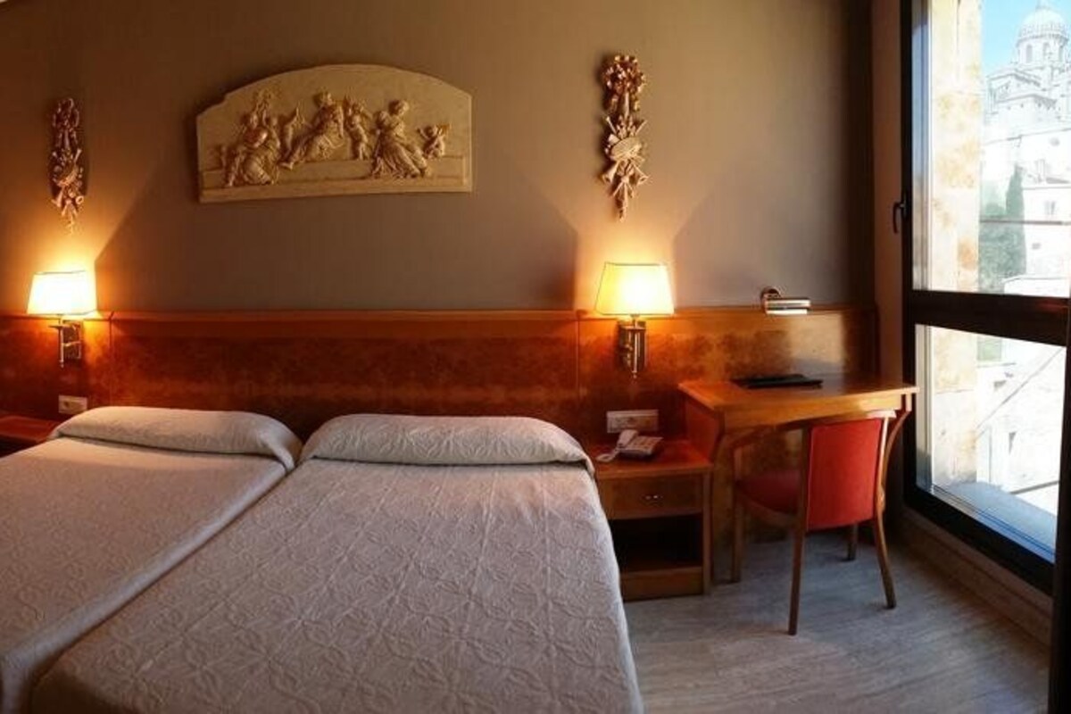 A hotel room with two beds, a desk, and a chair.