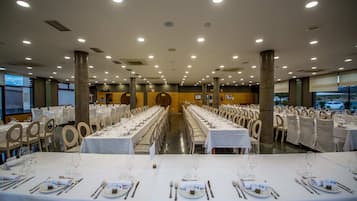 Un amplio salón de banquetes con largas mesas dispuestas para el servicio de comidas, con manteles blancos y cubertería impecable.