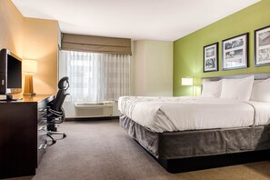 A hotel room with a bed, desk, chair, and air conditioning unit.