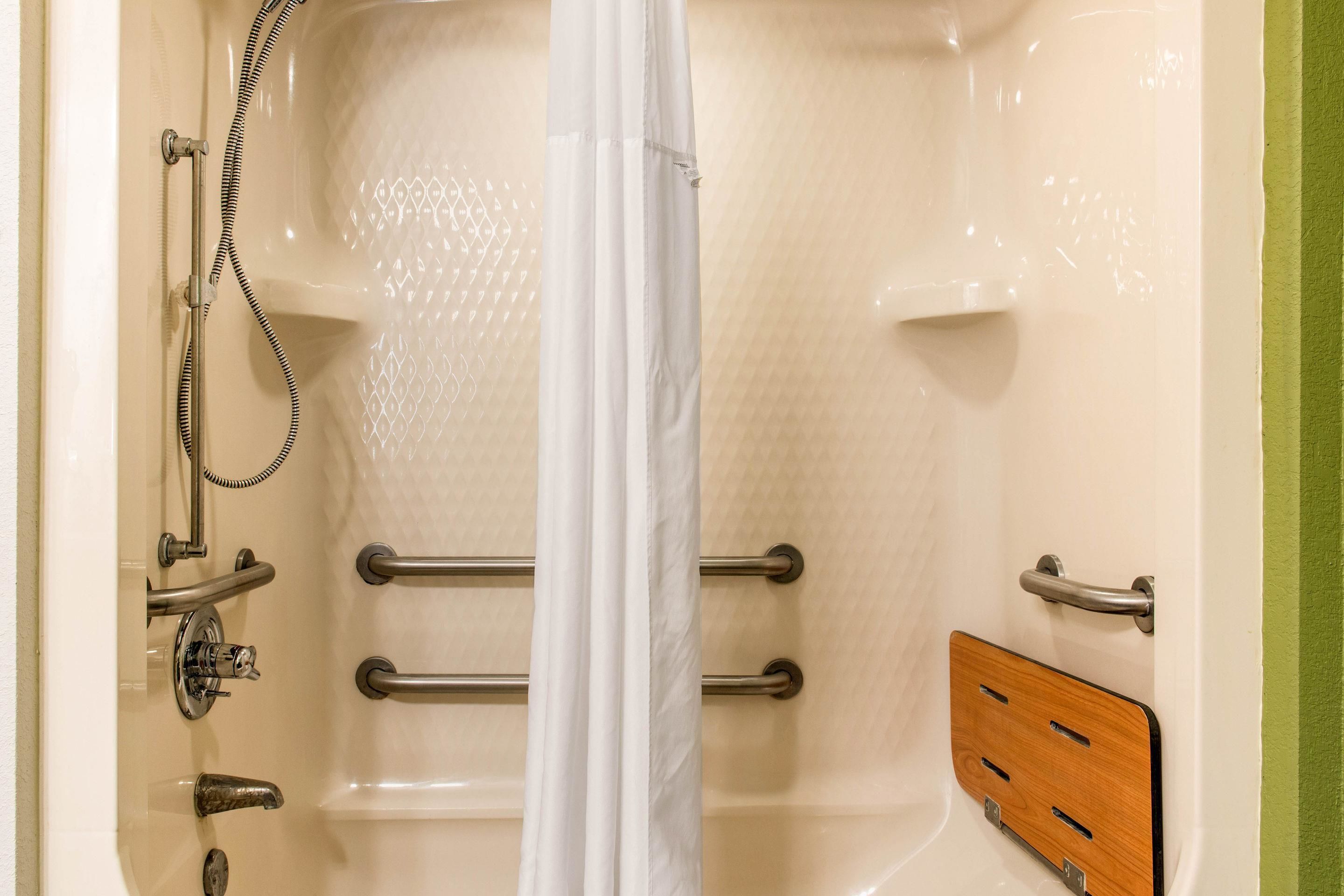 A bathtub with a showerhead, grab bars, and a wooden panel.