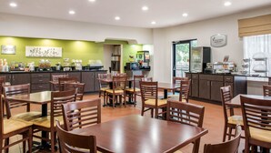 Un coin repas avec des tables et des chaises en bois, un espace cuisine agrémenté d’un mur vert, et une enseigne indiquant « Morning Medley ».