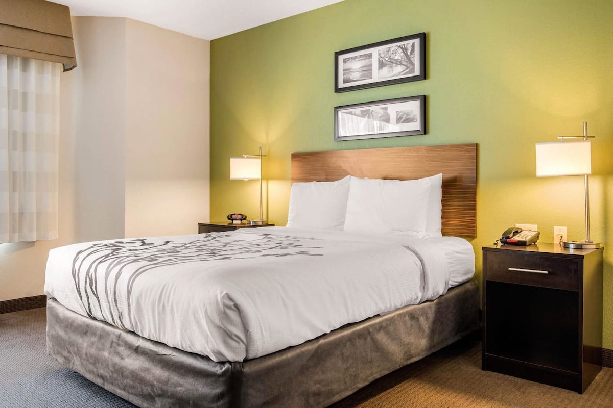 Une chambre d’hôtel avec un lit, deux tables de chevet avec des lampes, une tête de lit en bois et deux tableaux encadrés au mur.