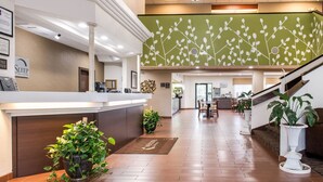 Un espace d’accueil d’hôtel au design moderne, comprenant un comptoir d’accueil, un escalier et, au fond, un espace repas.