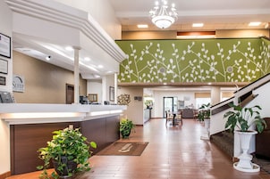 Zona de recepción de hotel con diseño moderno, que incluye un mostrador de recepción, una escalera y un área de comedor al fondo.