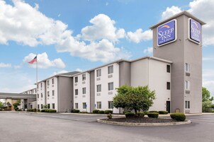 A Sleep Inn hotel with a modern design, featuring a central entrance, multiple windows, and a flagpole with an American flag.