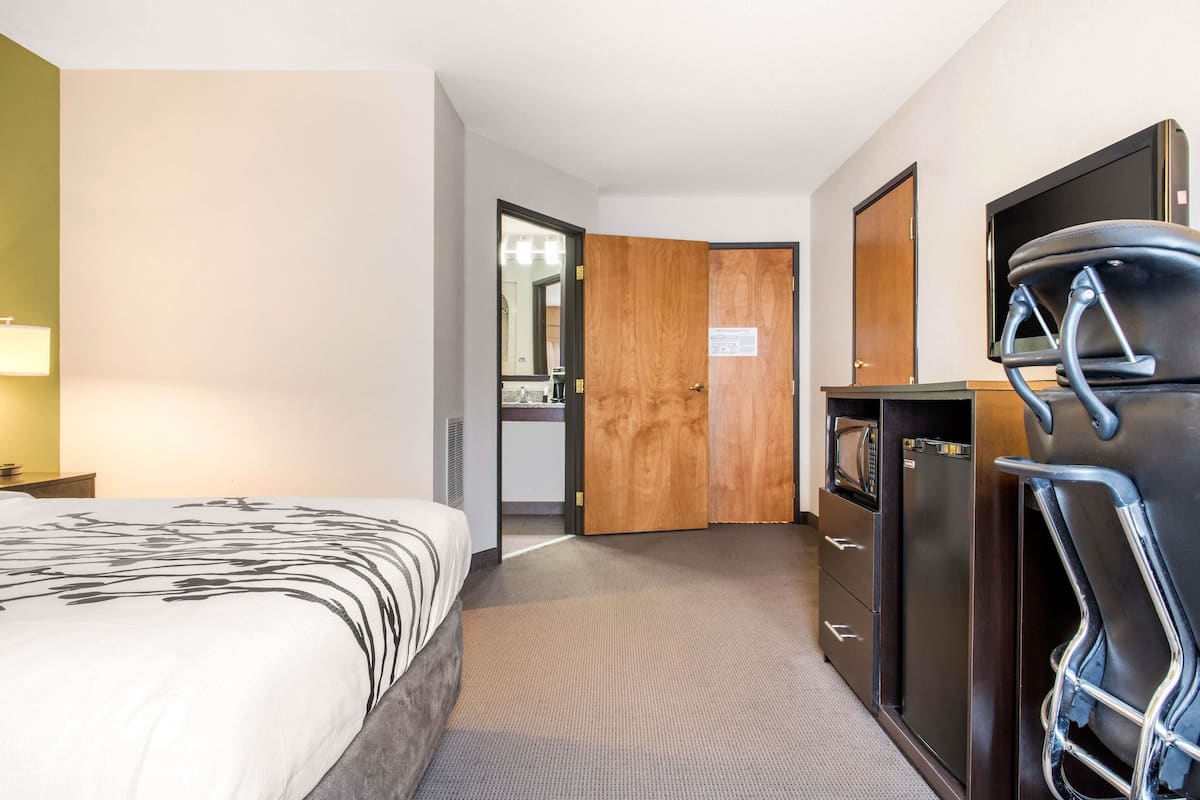 Une chambre d’hôtel comprenant un lit, une commode, un téléviseur et une porte donnant sur une salle de bain.