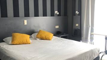 Habitación de hotel con una cama grande, dos almohadas, una mesita de noche, una lámpara y un ventanal con cortinas.