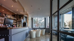 A bar area with a wooden counter, shelves with bottles, and a large window offering a view of trees.
