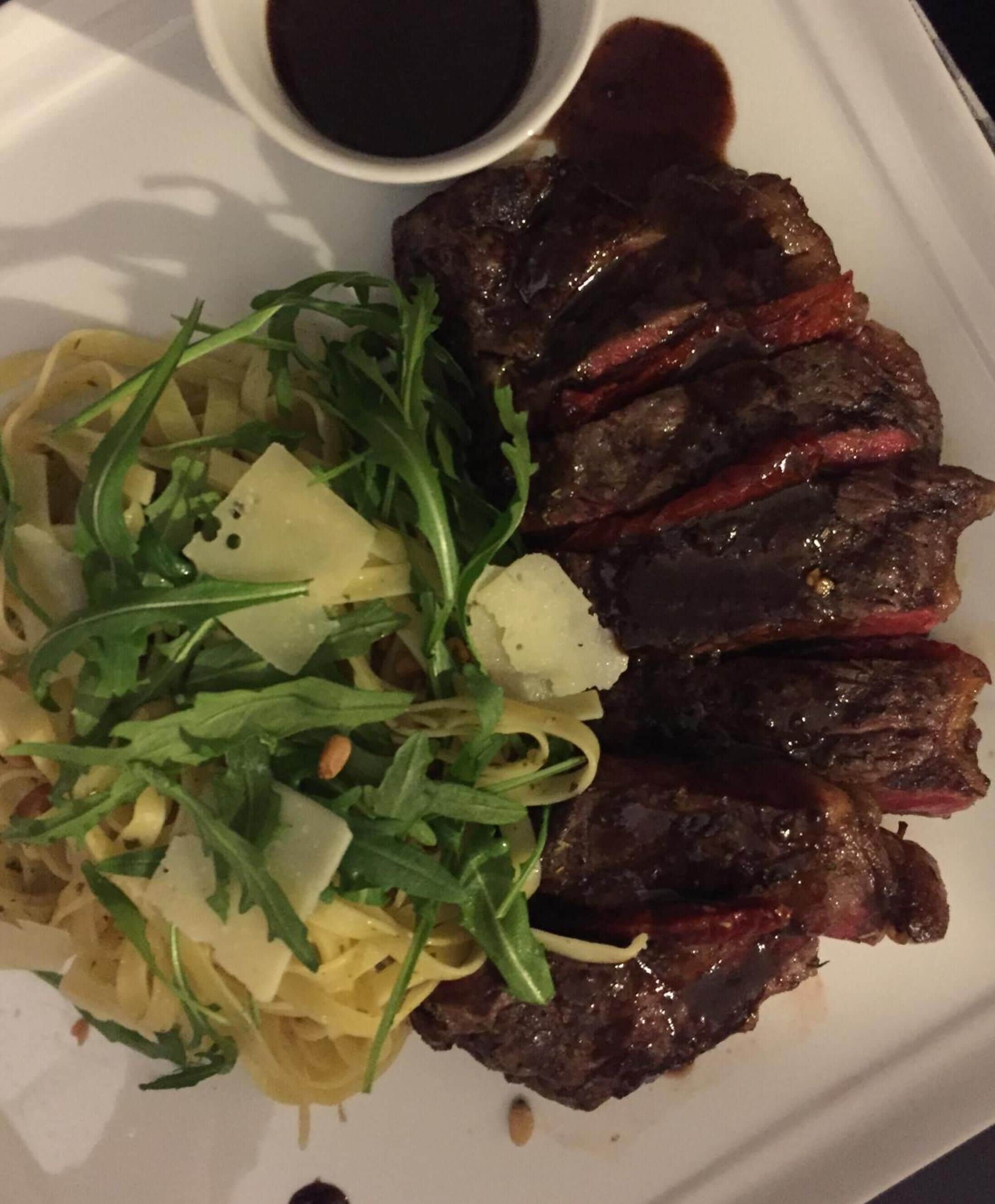 A plate with sliced meat, greens, and pasta.