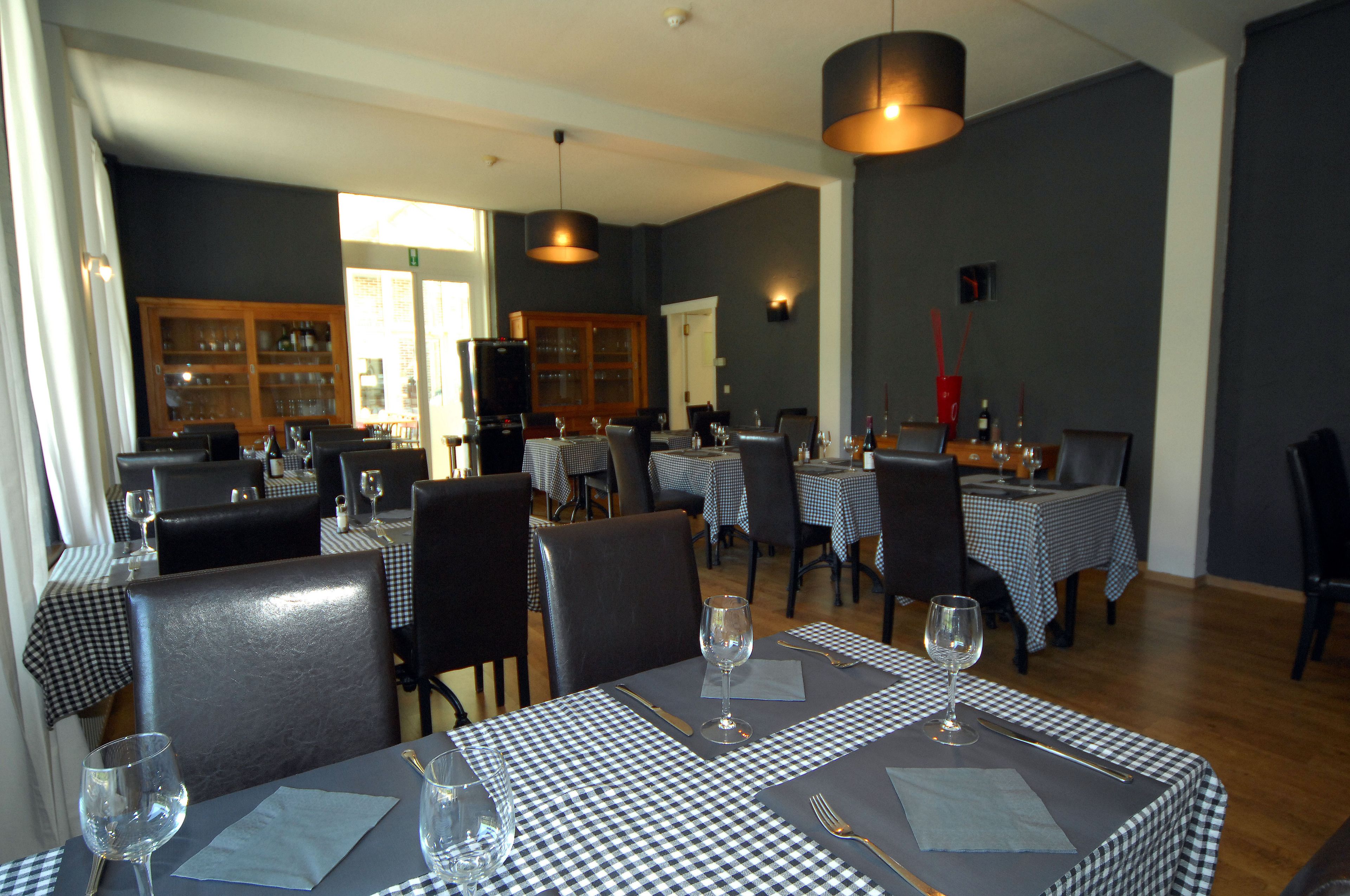 Un comedor con manteles a cuadros, sillas negras y copas de vino colocadas en cada mesa.