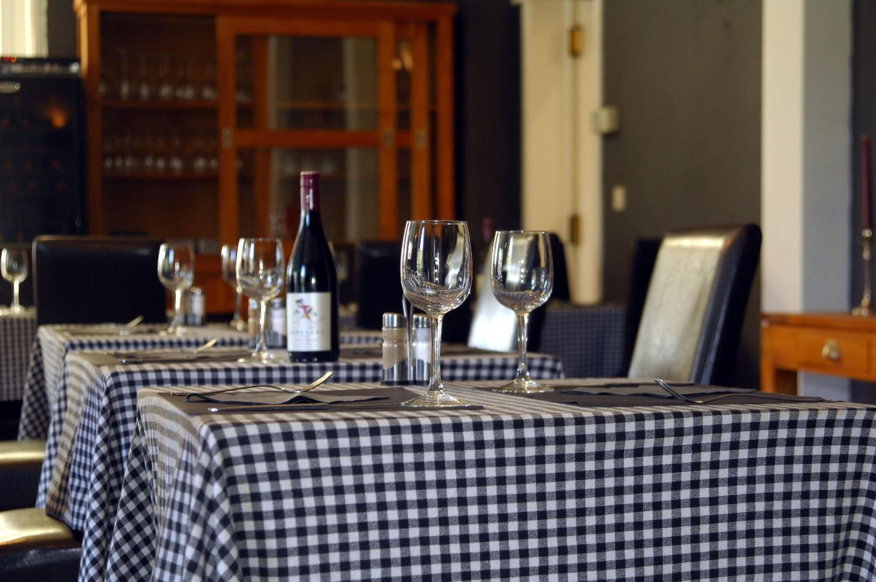 A dining area with checkered tablecloths, wine glasses, and a bottle of wine.
