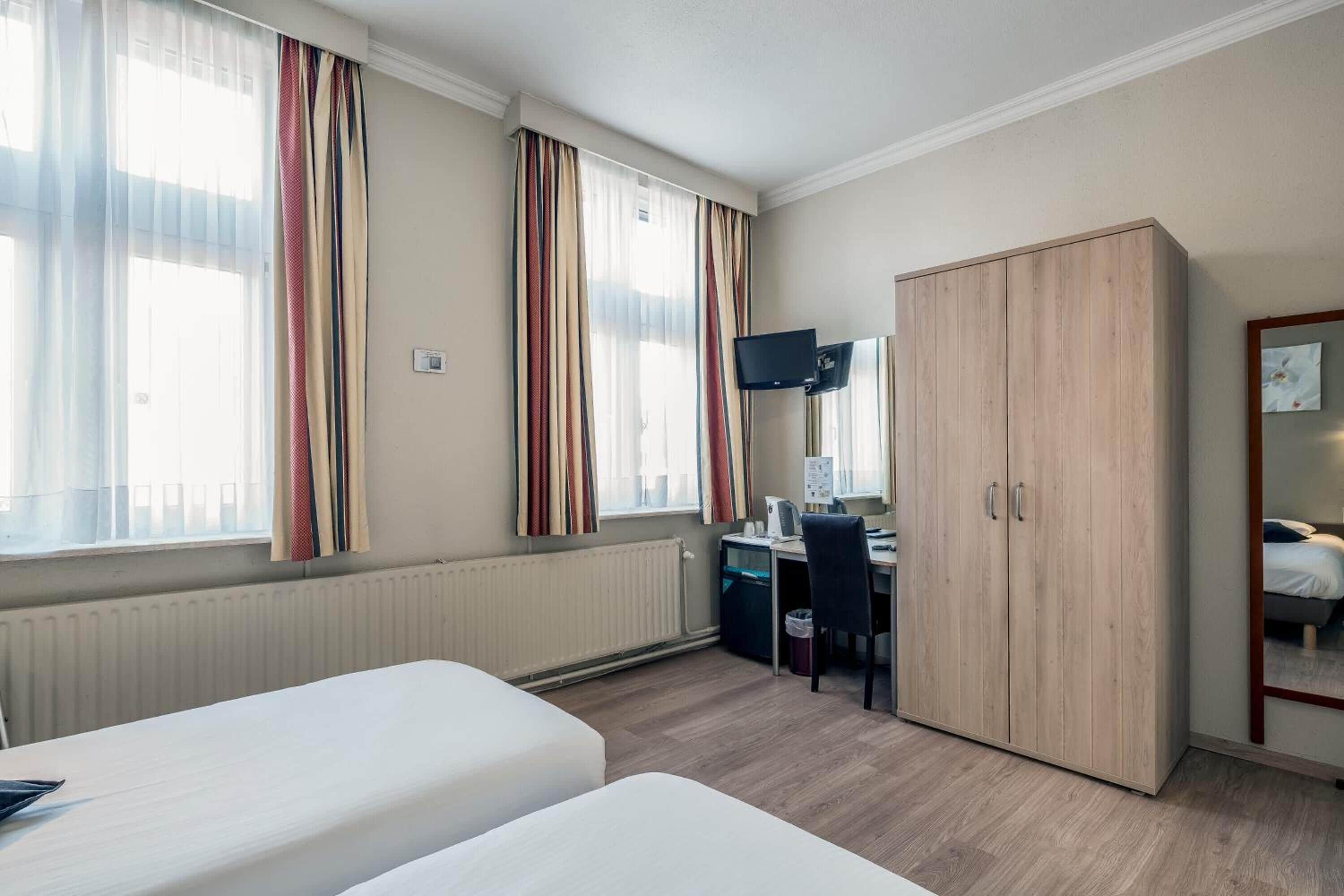 Una habitación de hotel con dos camas, un escritorio con ordenador, televisión y armario.