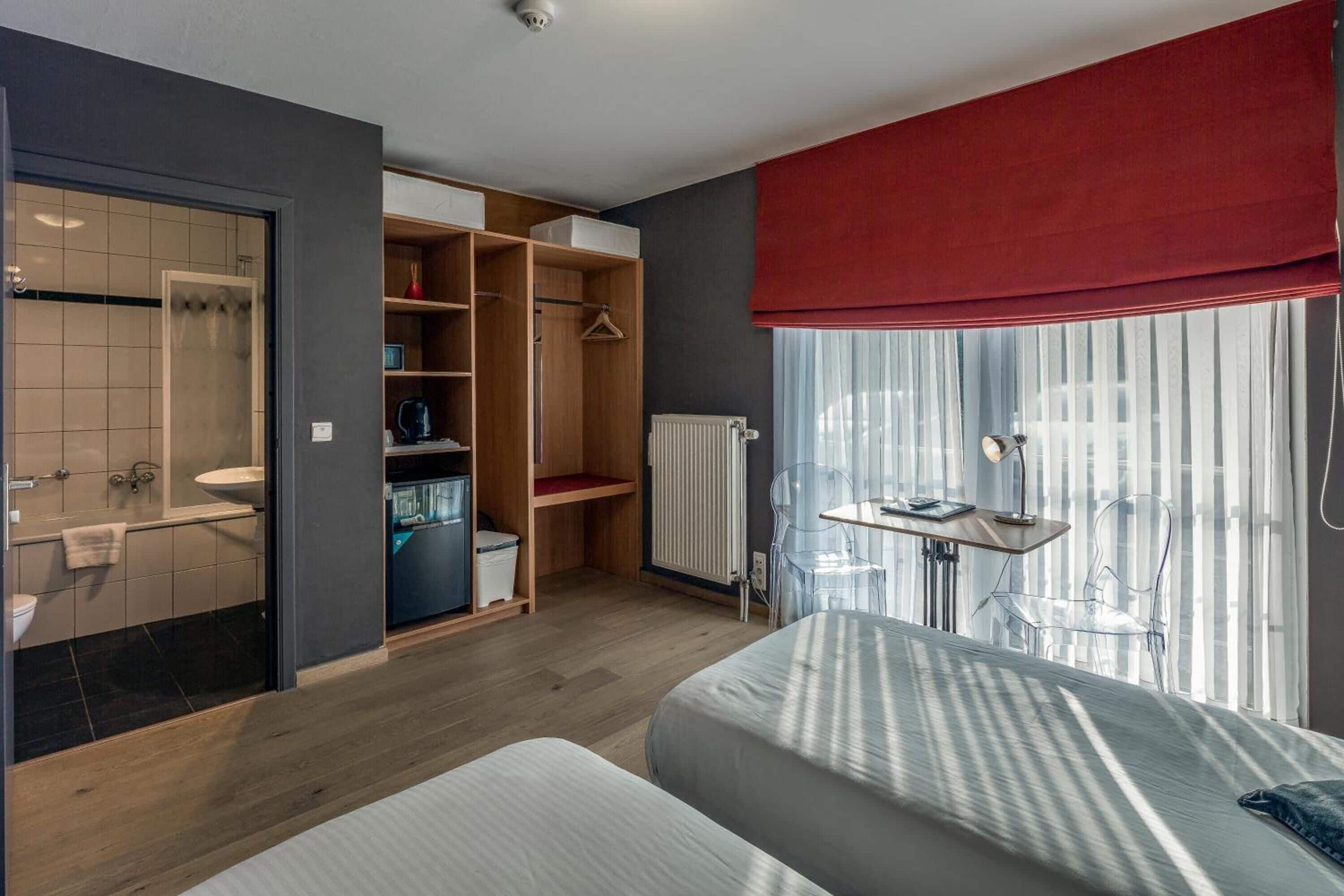 Een moderne hotelkamer met een houten vloer, een bed met gestreept beddengoed, een bureau met een stoel, een kledingkast en een badkamer met douche en toilet.