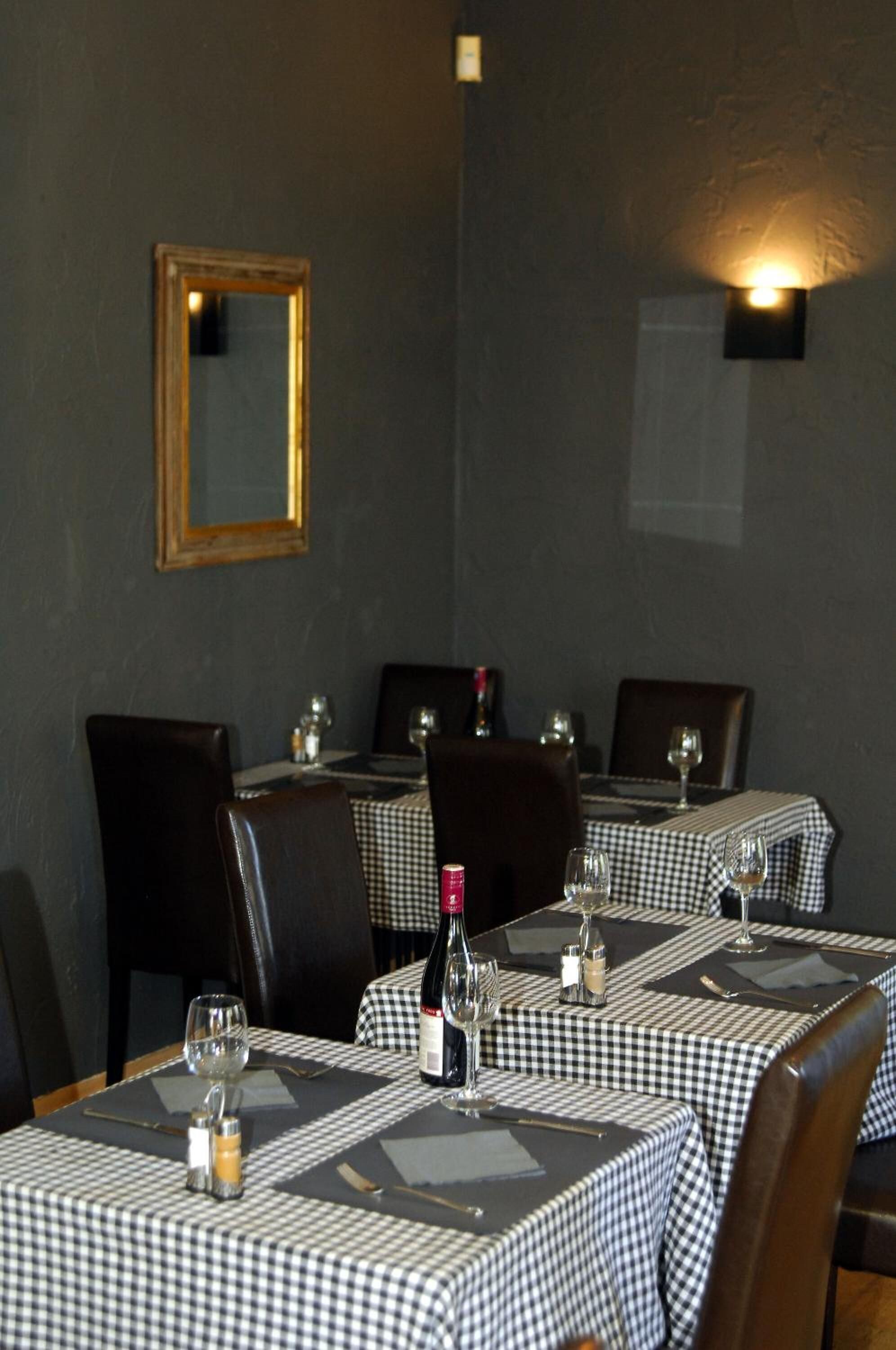 Un restaurant avec des nappes à carreaux, des chaises sombres et un miroir encadré accroché au mur.