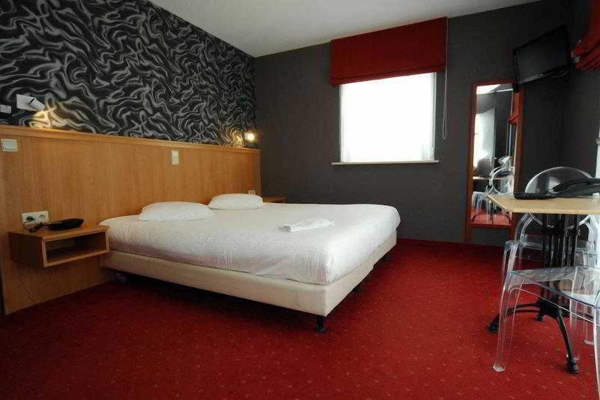 A hotel room with a bed, a desk, a chair, a mirror, and a window.
