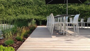 An outdoor patio with a wooden deck, white plastic chairs, and a table.