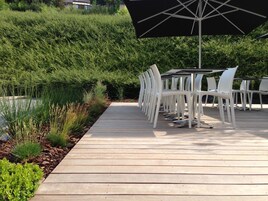 Un patio al aire libre con cubierta de madera, sillas de plástico blanco y una mesa.