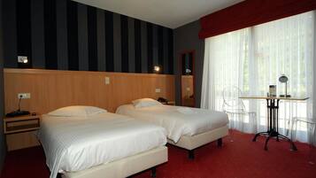 A hotel room with two beds, a desk with a chair, a mirror, and a window with curtains.