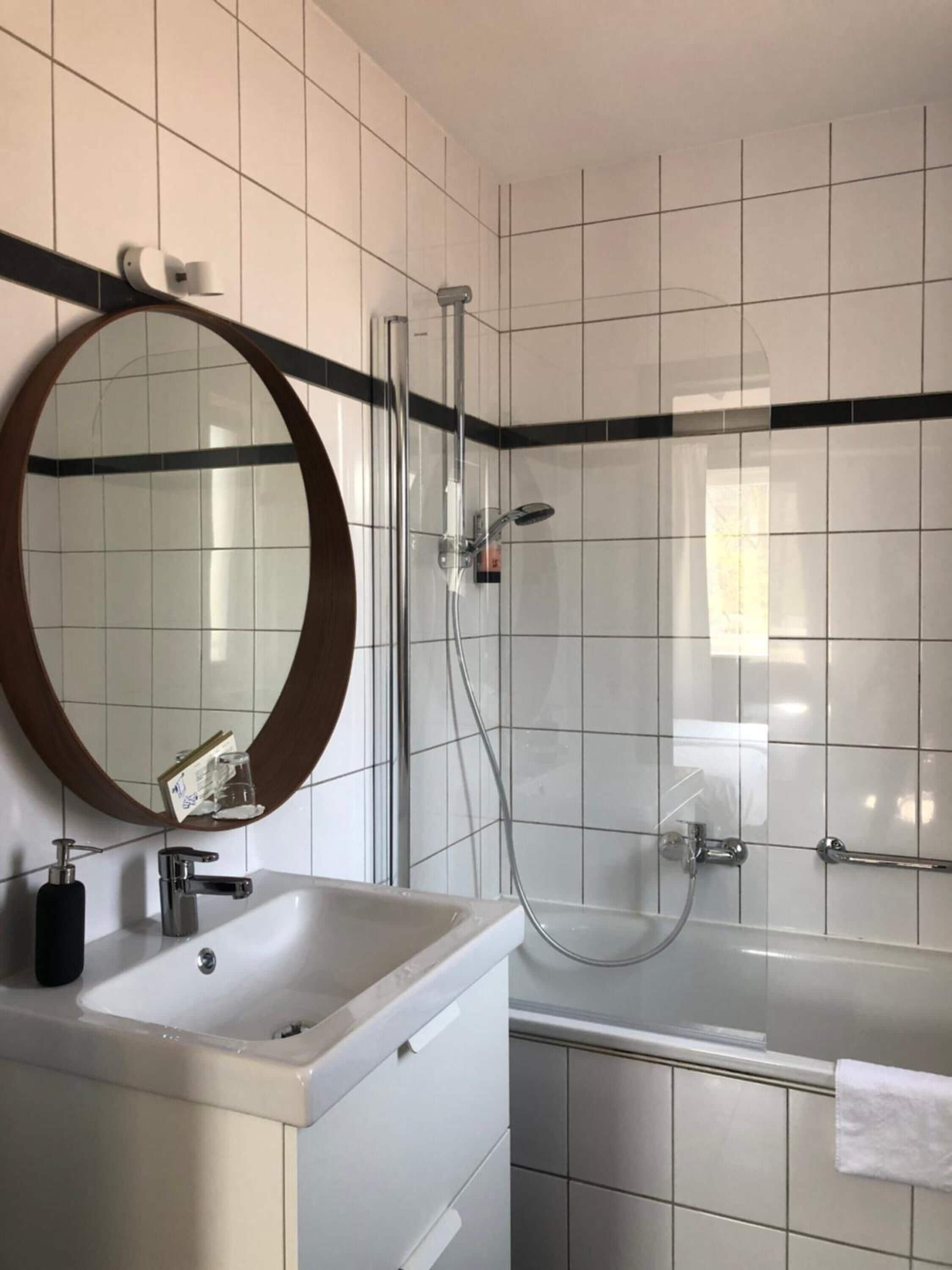 Un baño con lavamanos blanco, espejo y ducha.