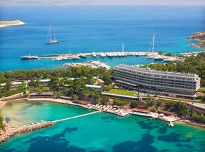 Un hotel frente al mar con un puerto deportivo, varias piscinas y un edificio grande con balcones.