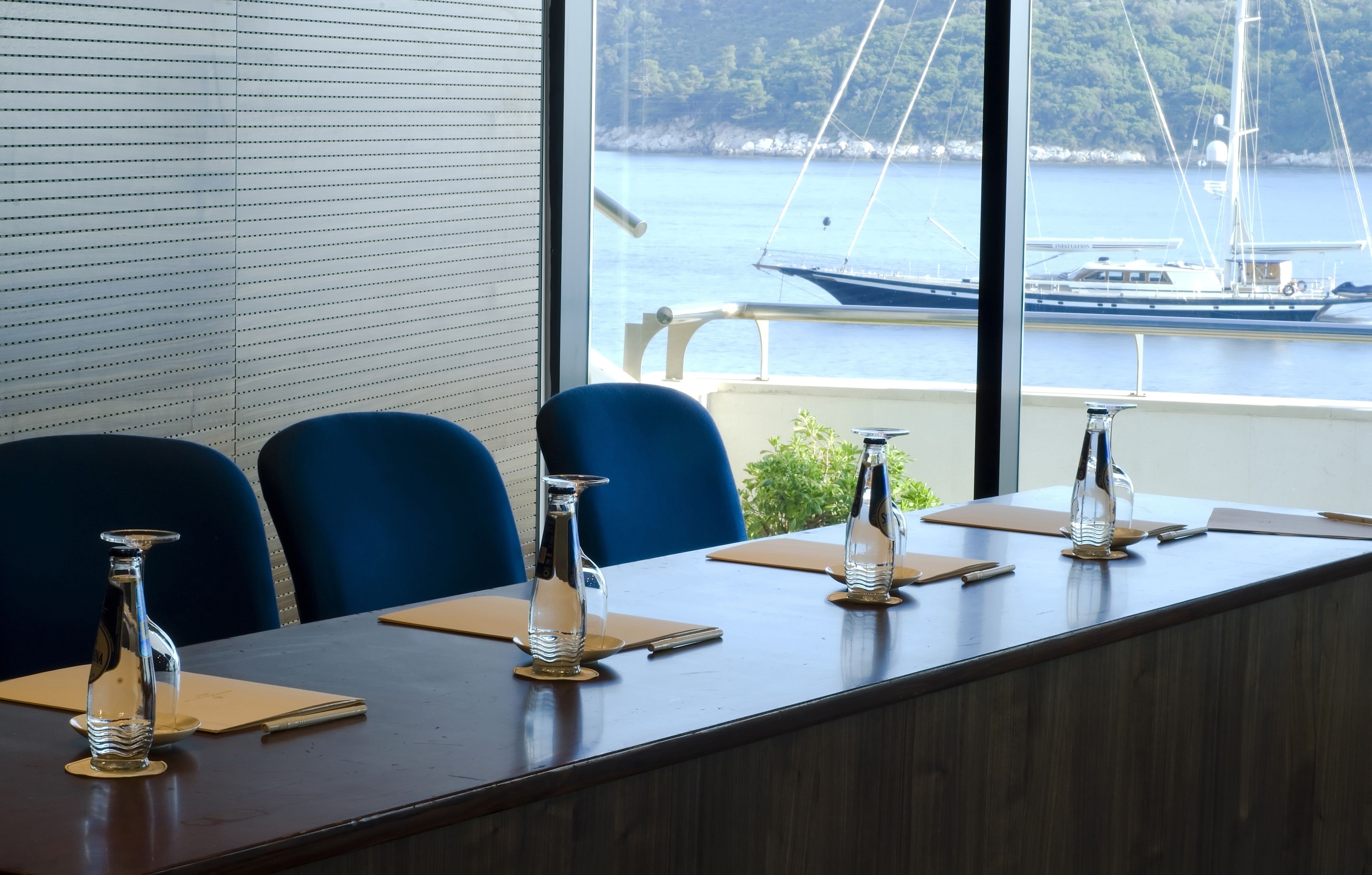 A conference room with a long table, blue chairs, and a view of a body of water with boats.