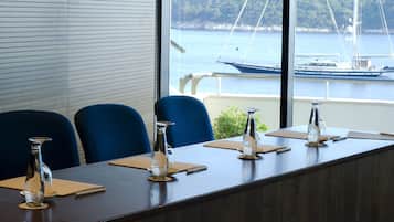 A conference room with a long table, blue chairs, and a view of a body of water with boats.